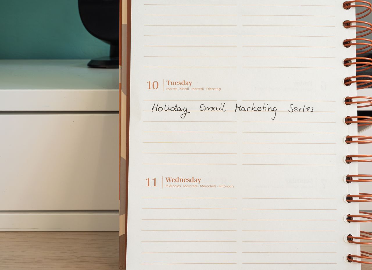 A planner open on a desk with a handwritten note reading Holiday Email Marketing Series.